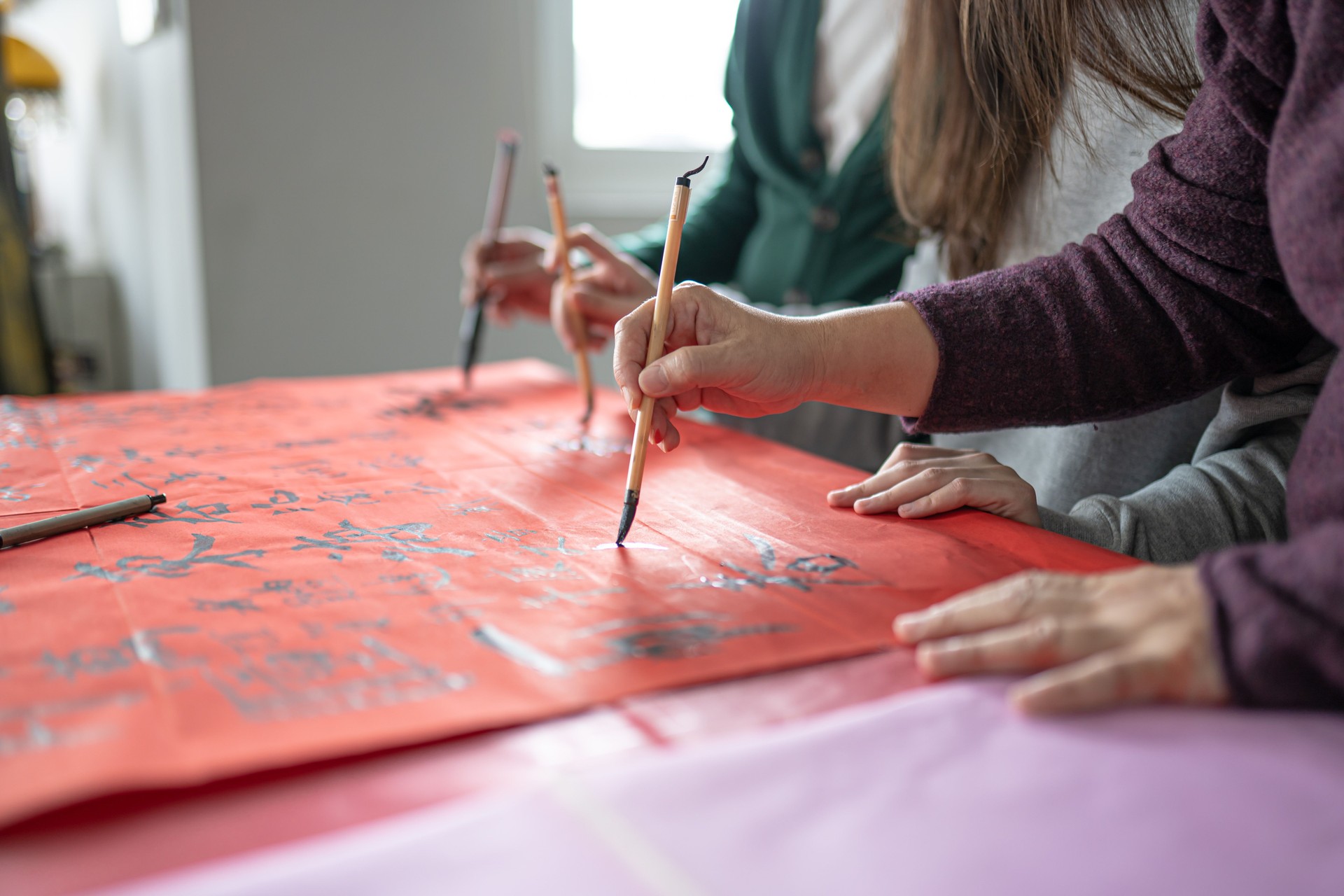 Asian Chinese family practicing Chinese calligraphy during Chinese new year celebration home decoration a red piece of paper